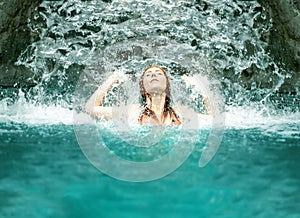 Beautiful young cute redhead woman in Bikini under the splashing water of the waterfall in the Spa Wellness pool and raises her