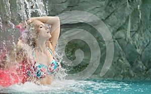 Beautiful young cute sexy blonde woman with closed eyes, raises her arms, enjoying the feeling of splashing water of the waterfall