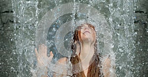 beautiful young cute sexy Portrait of a redhead woman with raised arm under the splashing pattering waterfall burbling water in