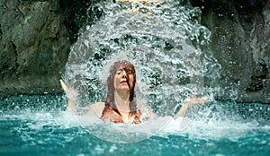 Beautiful young cute sexy redhead woman girl under the splashing falling water shower waterfall in the Spa Wellness pool