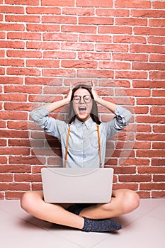 Beautiful young dark-haired girl in casual clothes with laptop, looking in camera and showing surprise