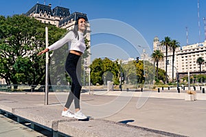 Beautiful young dark-haired Latin woman dancing and jumping in a square dressed casually with black jean and white top. Joy