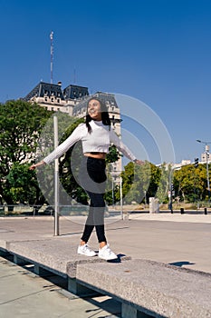 Beautiful young dark-haired Latin woman dancing and jumping in a square dressed casually with black jean and white top. Joy