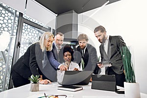 Beautiful young dark-skinned african female boss sitting at the table in office and listening to her diverse colleagues