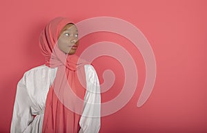 Beautiful young dark-skinned young woman of Arab appearance, looks sideways cheerfully, wears white shirt and pink veil, has