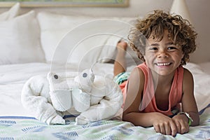 Beautiful young diverse boy sitting on bed in a cruise ship next to a towel animal