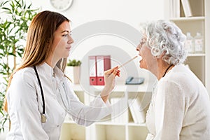 Beautiful young doctor examining throat to senior woman