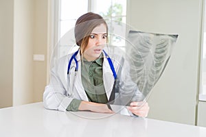 Beautiful young doctor woman looking at chest radiography scared in shock with a surprise face, afraid and excited with fear