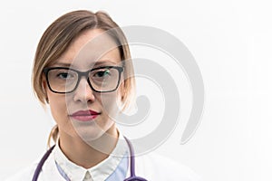 Beautiful young doctor woman in a medical coat and glasses with a stethoscope in a hospital on a white background