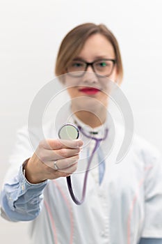 Beautiful young doctor woman in a medical coat and glasses with a stethoscope in a hospital on a white background.
