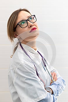 Beautiful young doctor woman in a medical coat and glasses with a stethoscope in a hospital on a white background