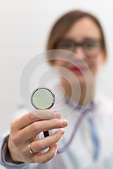 Beautiful young doctor woman in a medical coat and glasses with a stethoscope in a hospital on a white background