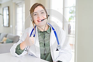 Beautiful young doctor woman wearing headset doing happy thumbs up gesture with hand