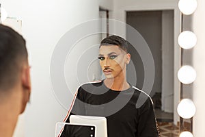 Young drag queen makeup artist looking at himself in front of the mirror