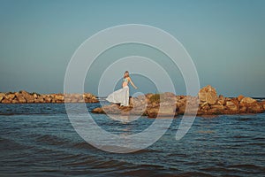 Beautiful young elegant pregnant blond woman in a blue hat walks on the beach, seashore at sunset. sea. Motherhood.