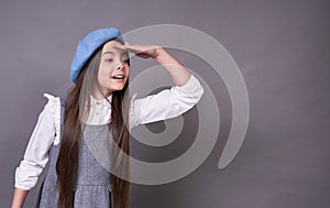 Beautiful young emotional lady in a stylish blue hat in a beret on a gray background