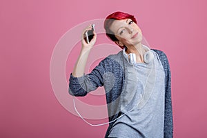 Girl with red hair listening to music on headphones raising her hand up holding the phone.
