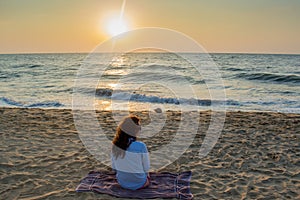 Beautiful young european woman sitting on the beach near ocean during sunset