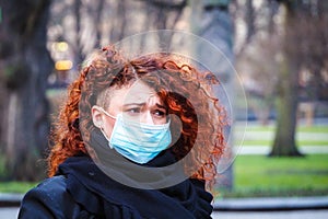 Beautiful young European woman in spring clothes on the street with a medical face mask on