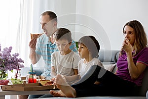 Beautiful young family with children, eating pizza at home and watching TV