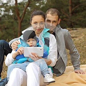 Beautiful young family lying on a blanket and looking at tablet