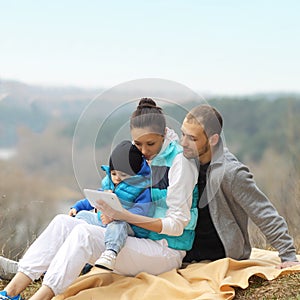 Beautiful young family lying on a blanket and looking at tablet