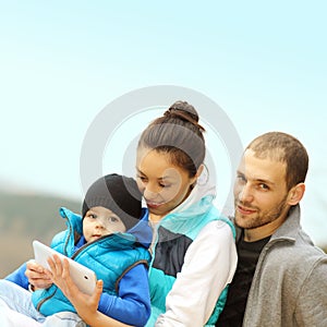 Beautiful young family lying on a blanket and looking at tablet.