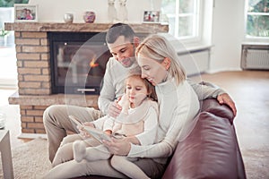 Beautiful young family is reading a book near the fireplace. Cozy