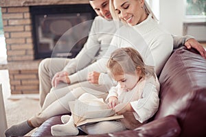 Beautiful young family is reading a book near the fireplace. Cozy