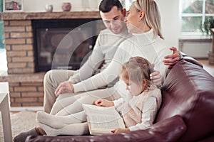 Beautiful young family is reading a book near the fireplace. Cozy