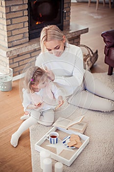 Beautiful young family is reading a book near the fireplace. Cozy