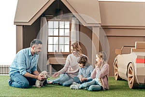 beautiful young family sitting on yard of cardboard house