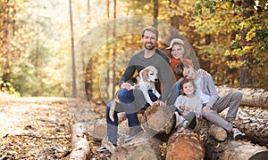 Beautiful young family with small children and dog sitting in autumn forest.