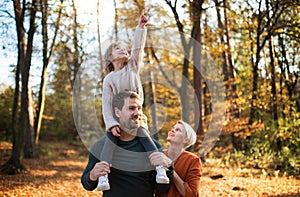 Beautiful young family with small daughter on a walk in autumn forest.