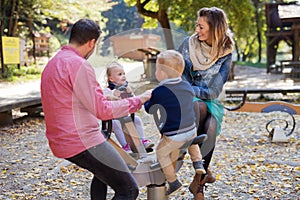 Beautiful young family with small twins playing on playground in autumn.