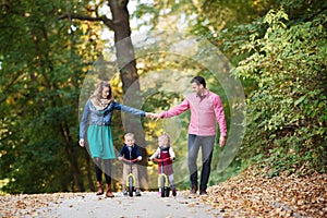 Beautiful young family with small twins on a walk in autumn forest.