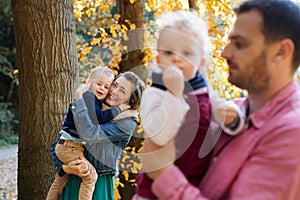 Beautiful young family with small twins on a walk in autumn forest.