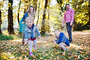 Beautiful young family with small twins on a walk in autumn forest, playing.