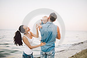 Beautiful young family on vacation with baby. The father holds the blonde girl in her arms, and the brunette`s mother hugs her