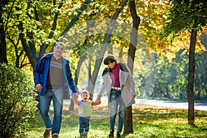 Beautiful young family on a walk in autumn forest on maple yellow trees background. Father and mother hold son on hands. Happy