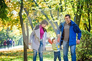 Beautiful young family on a walk in autumn forest on maple yellow trees background. Father and mother hold son on hands. Happy