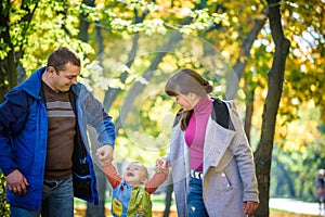 Beautiful young family on a walk in autumn forest on maple yellow trees background. Father and mother hold son on hands. Happy fa