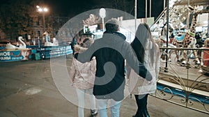 A beautiful young family is walking in the evening in the amusement park. Family vacation in the lunapark.