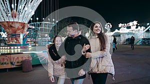 A beautiful young family walks at night in the amusement park amidst luminous attractions.