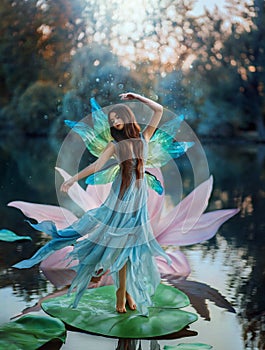 Beautiful young fantasy woman in the image of a river fairy dances on a water lily flower. A long silk dress flies in