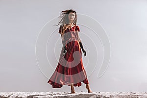 Beautiful young fashionable woman in elegant dress at the beach at sunset