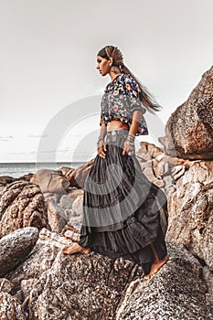Beautiful young fashionable woman on the rocks at sunset