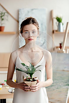 beautiful young female artist holding green potted plant and looking