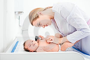 Beautiful young female blonde doctor examining little baby with ear speculum in clinic. Baby health concept photo