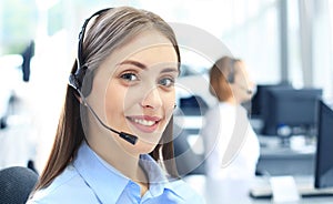 Beautiful young female call center operator with headset in office.